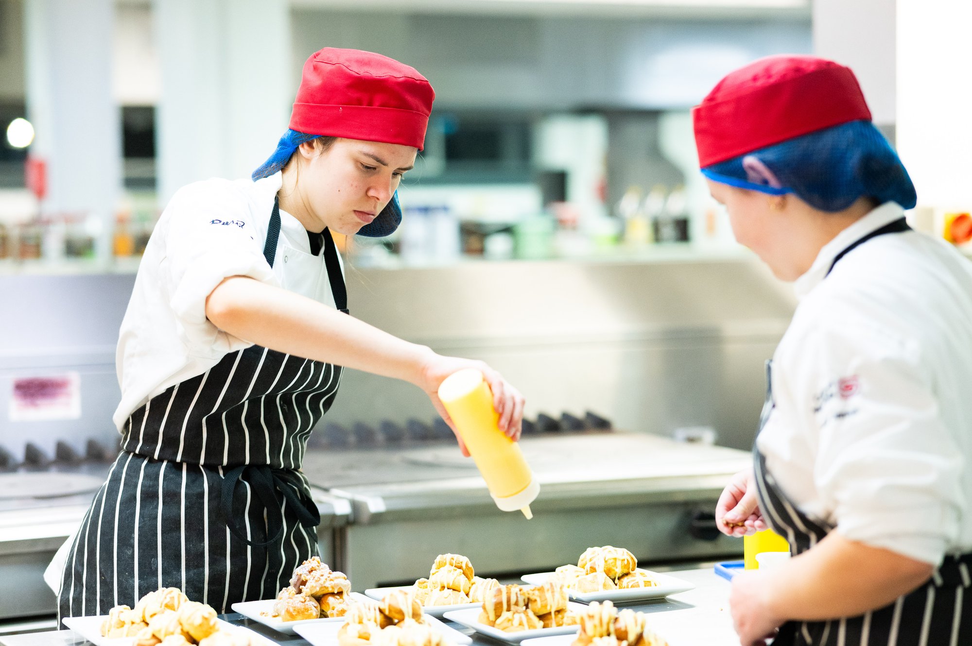 two students in the kitchen preparing deserts by putting sauce on them
